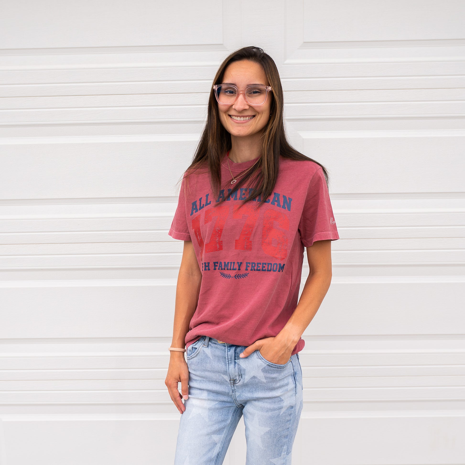 Woman wearing red 1776 All American t-shirt smiling against white background