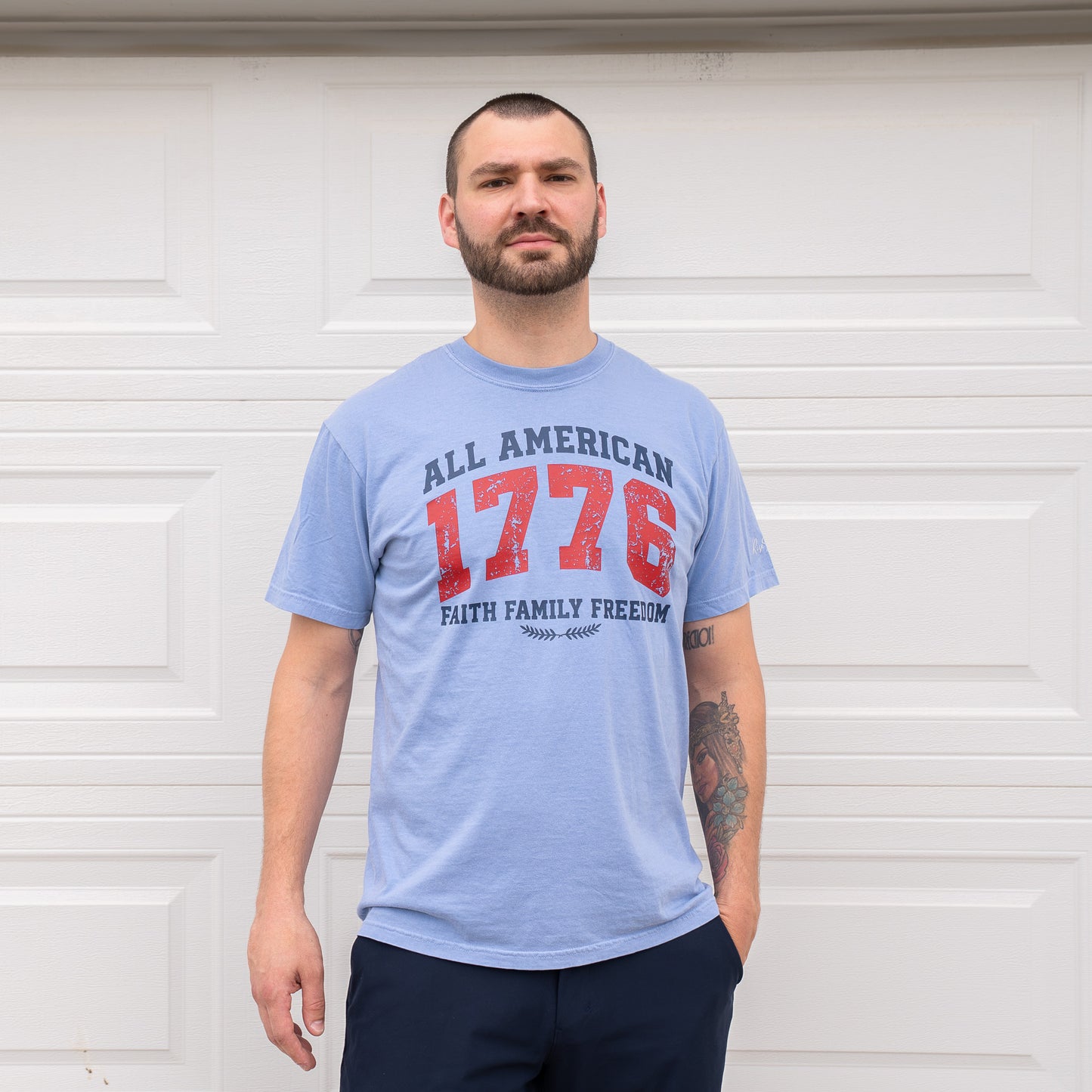 Man standing confidently wearing blue 1776 t-shirt with tattooed arms