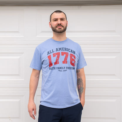 Man standing confidently wearing blue 1776 t-shirt with tattooed arms