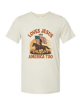Beige patriotic and Christian t-shirt with graphic of a person on a horse, American flag, and text 'LOVES JESUS AND AMERICA TOO' on a white background.