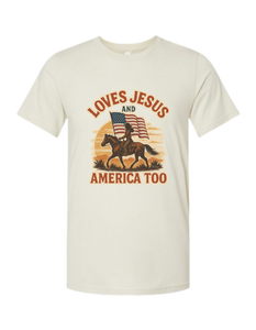 Beige patriotic and Christian t-shirt with graphic of a person on a horse, American flag, and text 'LOVES JESUS AND AMERICA TOO' on a white background.