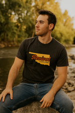 Man wearing a charcoal Christian t-shirt with 'Revival Starts Here' design, sitting by a body of water.