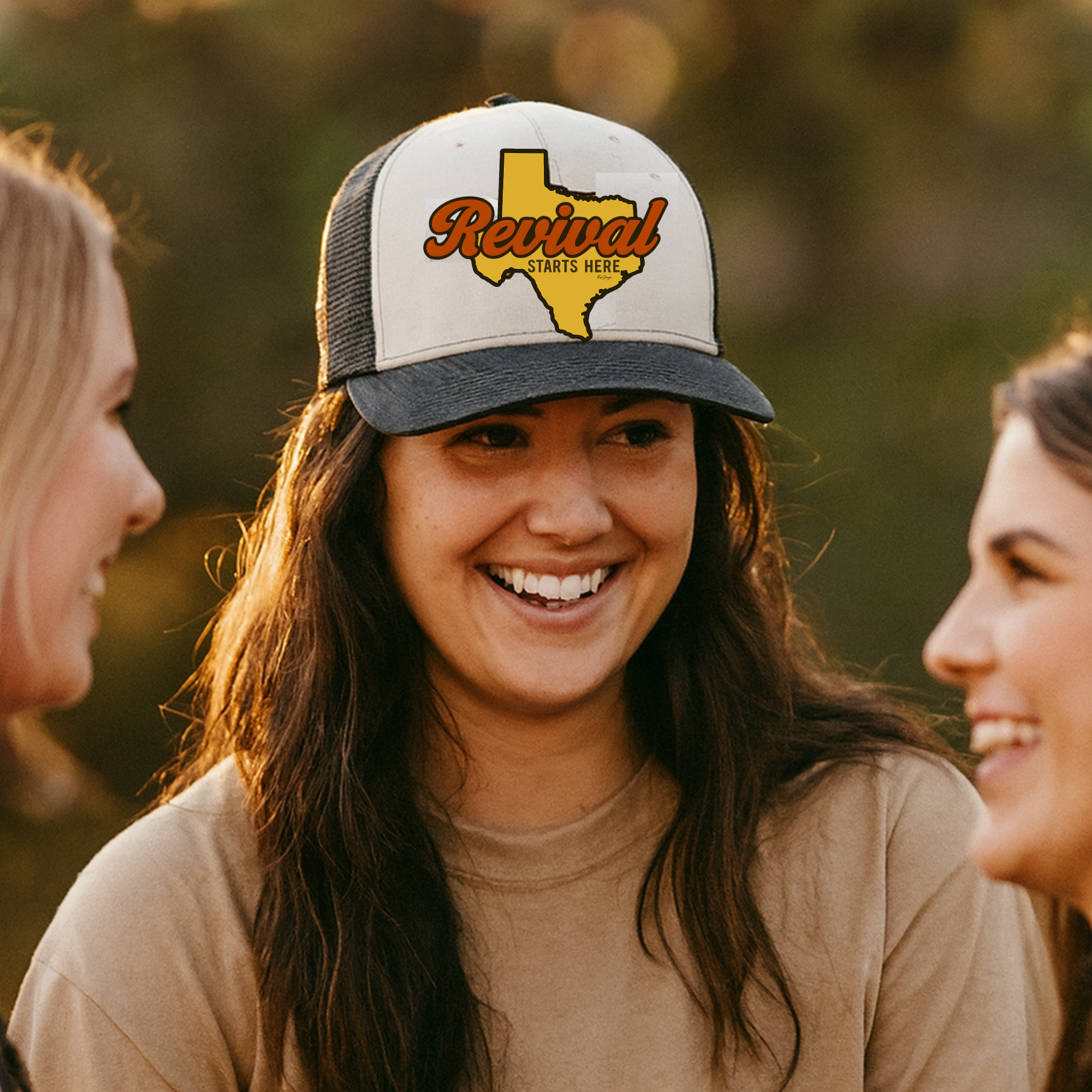 Woman wearing a cap with 'Revival Starts Here' Texas, surrounded by two other people outdoors.