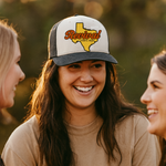 Woman wearing a cap with 'Revival Starts Here' Texas, surrounded by two other people outdoors.