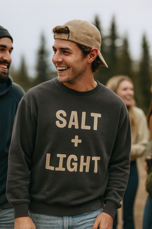 Man wearing a 'SALT + LIGHT' sweatshirt outdoors with trees in the background