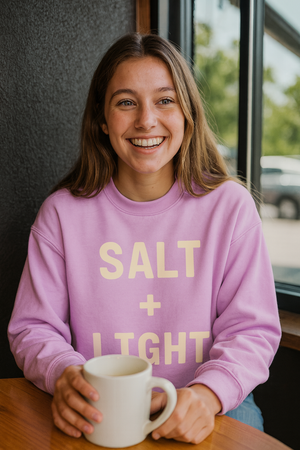 Young woman wearing a 'Salt + Light' crewneck sweatshirt.