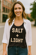 Christian woman wearing a black tank top and white cover-up with 'SALT + LIGHT' text, standing outdoors.
