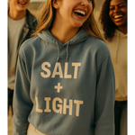 Young Christian woman wearing a 'SALT + LIGHT' hoodie with two friends in the background.