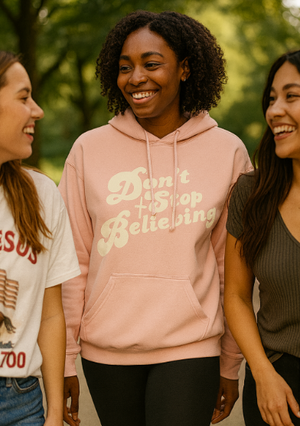 Three women standing outdoors, with one wearing a peach Christian hoodie with text that reads 'Don't Stop Believing.'