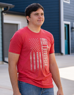 Man wearing a red Christian Patriotic with tattered American flag, a cross and Rise Stronger on the front in cream color.