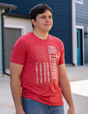 Man wearing a red Christian Patriotic with tattered American flag, a cross and Rise Stronger on the front in cream color.