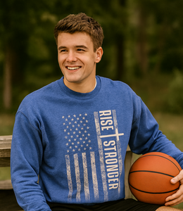 Male wearing a Christian crewneck sweatshirt with tattered American flag and Rise Stronger on the front in cream color over a royal blue garment.