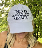 Woman wearing a white cap with 'THIS IS AMAZING GRACE' embroidered on the front in blue,