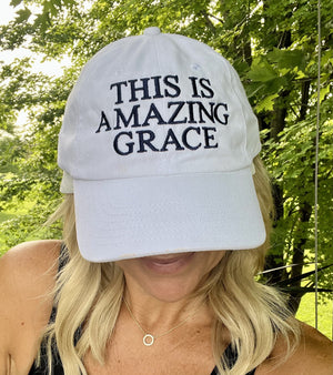 Woman wearing a white cap with 'THIS IS AMAZING GRACE' embroidered on the front in blue,